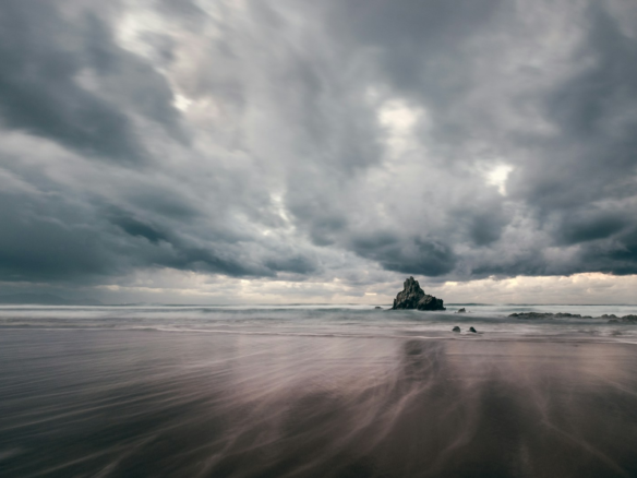 black rock formation on sea under gray clouds
