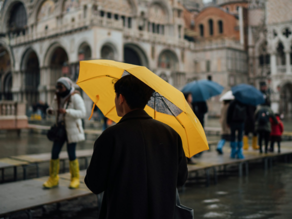 man in black coat holding yellow umbrella