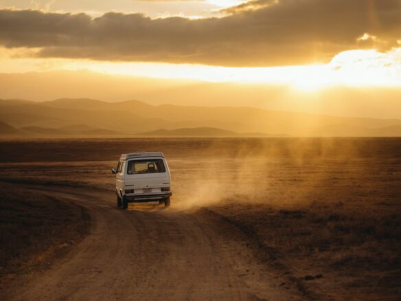 white vehicle traveling desert land field during sunset