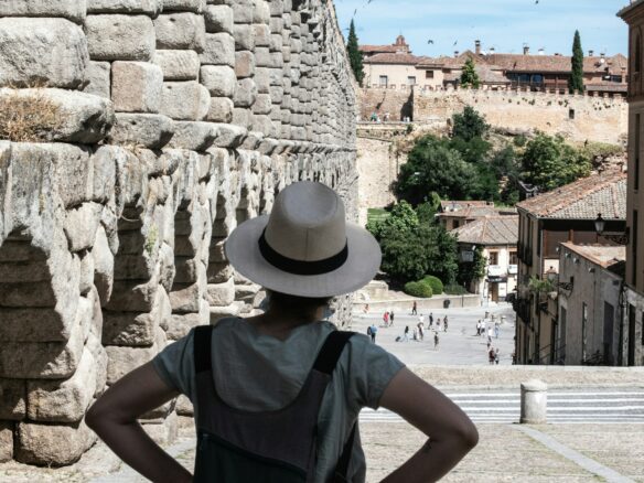 woman in blue crew neck t-shirt and brown fedora hat standing near brown concrete building