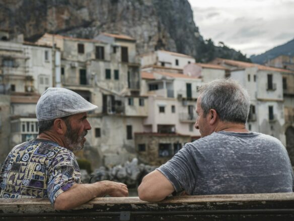 two men sitting on bench talking near village during day