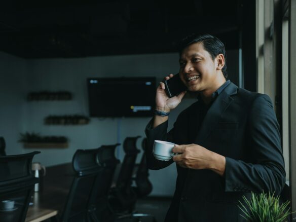 smiling man holding cup and using smartphone