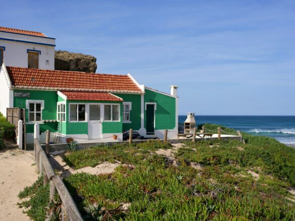A charming green house sits by the ocean.