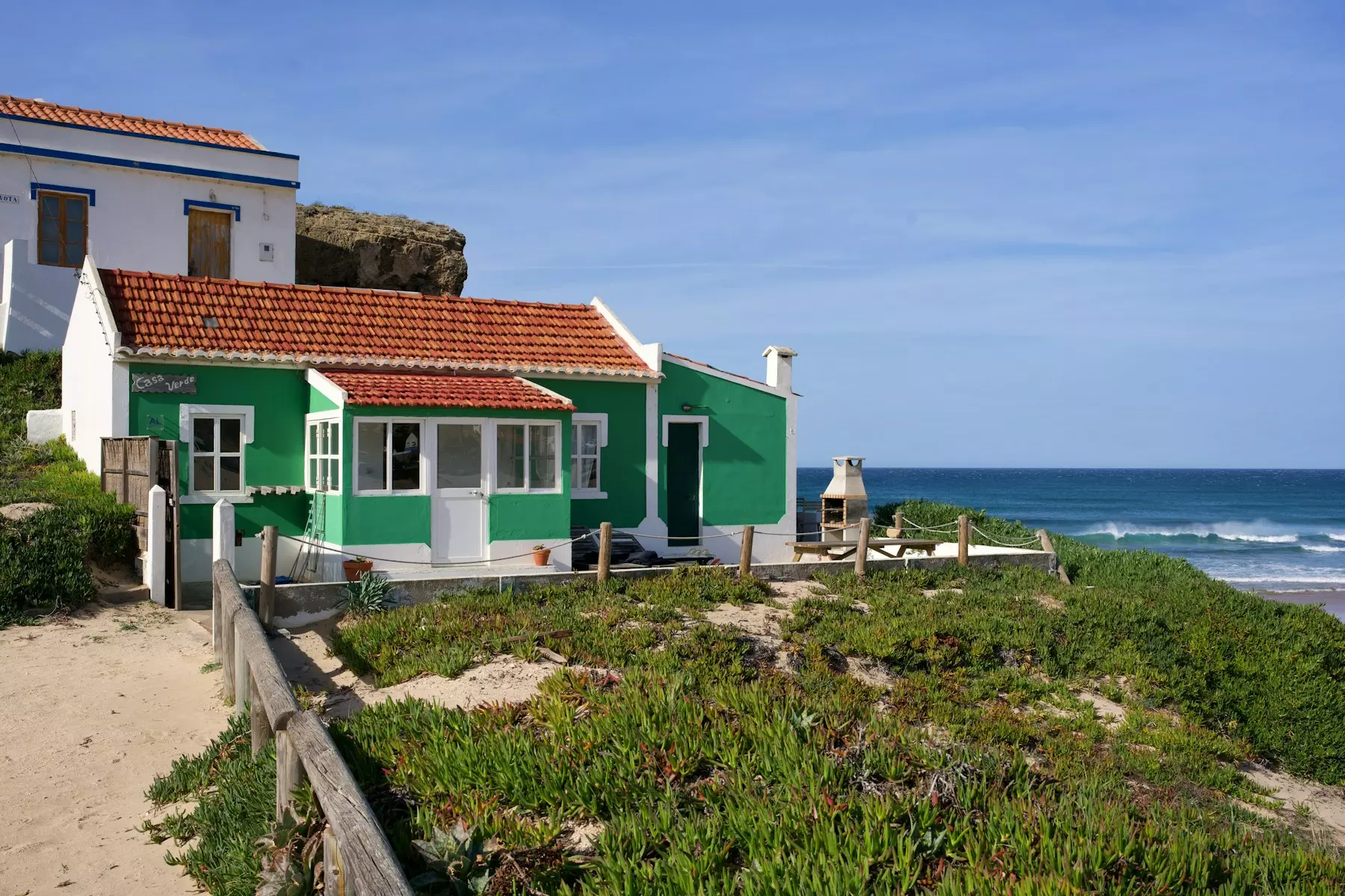 A charming green house sits by the ocean.