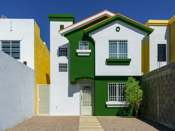 a green and white house sitting next to a white fence