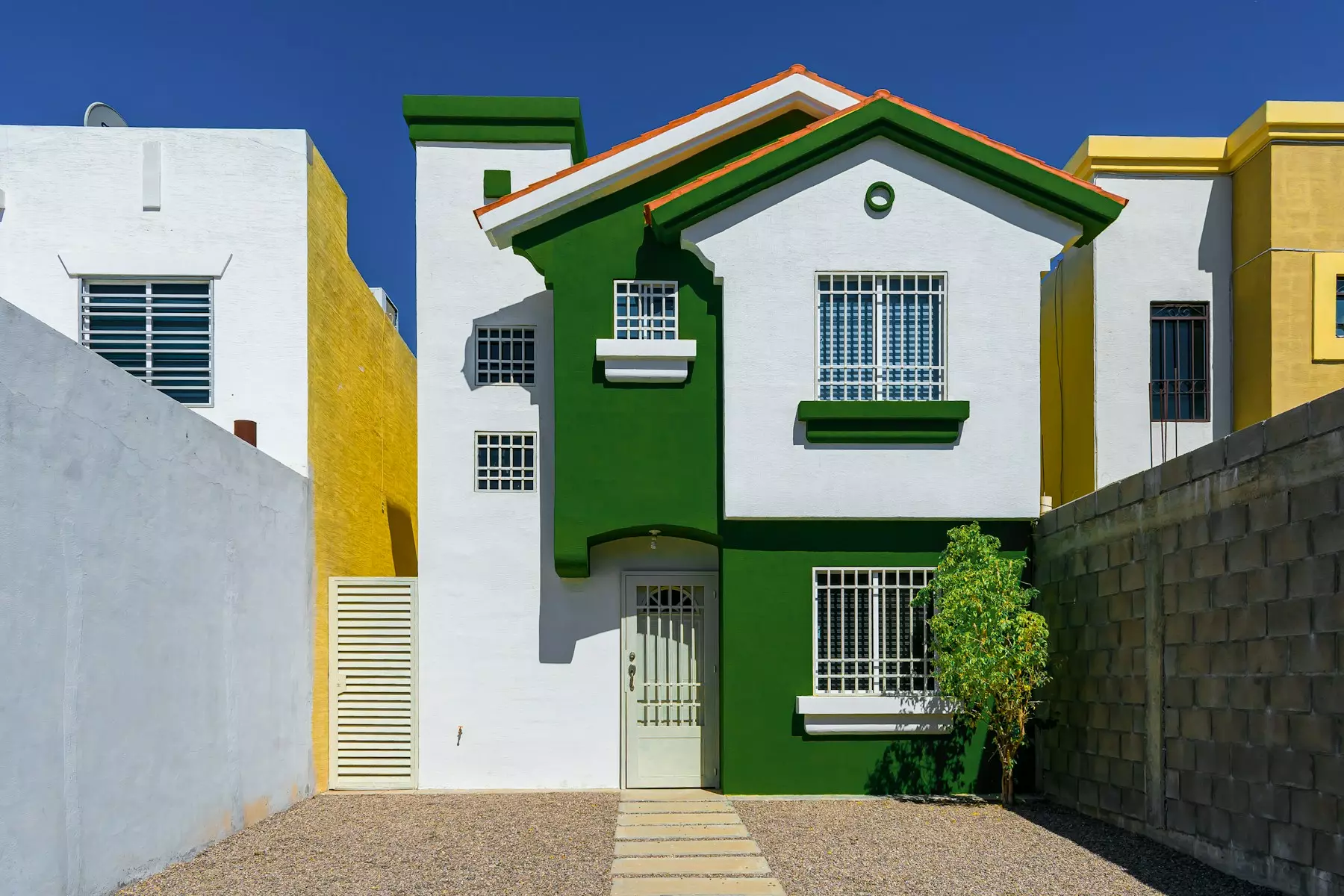 a green and white house sitting next to a white fence