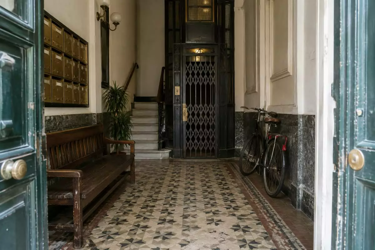 The tiled entrance hall of an old Madrid apartment building with an iron lift and brass letterboxes (illustration)