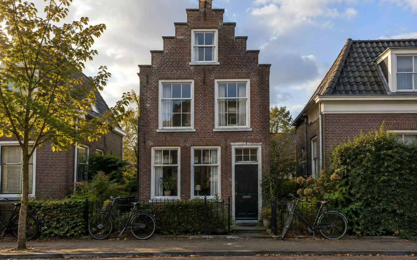 A narrow brick house with tall windows on a quiet Dutch street in early autumn (illustration)
