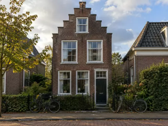 A narrow brick house with tall windows on a quiet Dutch street in early autumn (illustration)