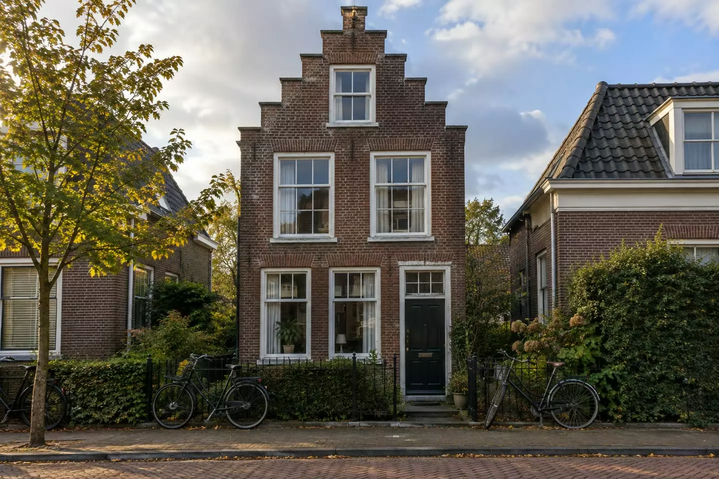 A narrow brick house with tall windows on a quiet Dutch street in early autumn (illustration)