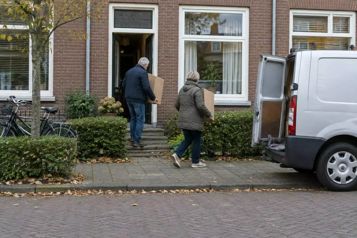 An older couple carrying moving boxes to a van outside a Dutch terraced house (illustration)