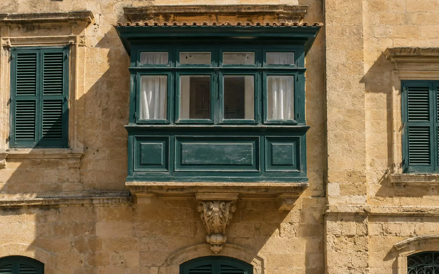 A traditional Maltese limestone balcony with a painted wooden box and shutters on a townhouse facade in early autumn (illustration)