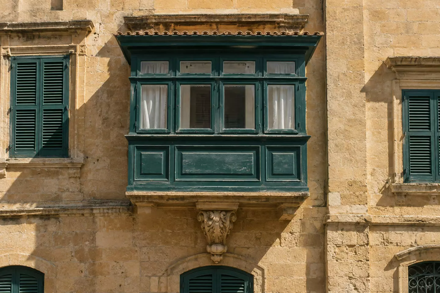 A traditional Maltese limestone balcony with a painted wooden box and shutters on a townhouse facade in early autumn (illustration)