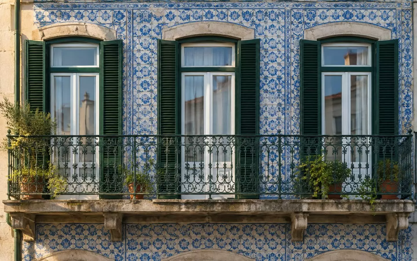 A Lisbon building facade with blue and white azulejo tiles and a wrought-iron balcony in early autumn (illustration)