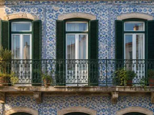 A Lisbon building facade with blue and white azulejo tiles and a wrought-iron balcony in early autumn (illustration)