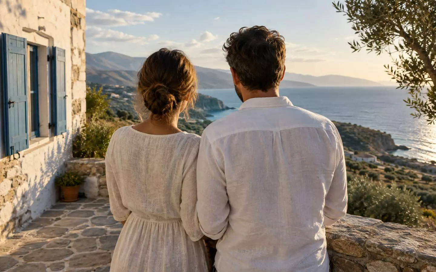 A couple seen from behind looking out to sea from the stone terrace of a whitewashed house in Crete, Greece, in early October (illustration)