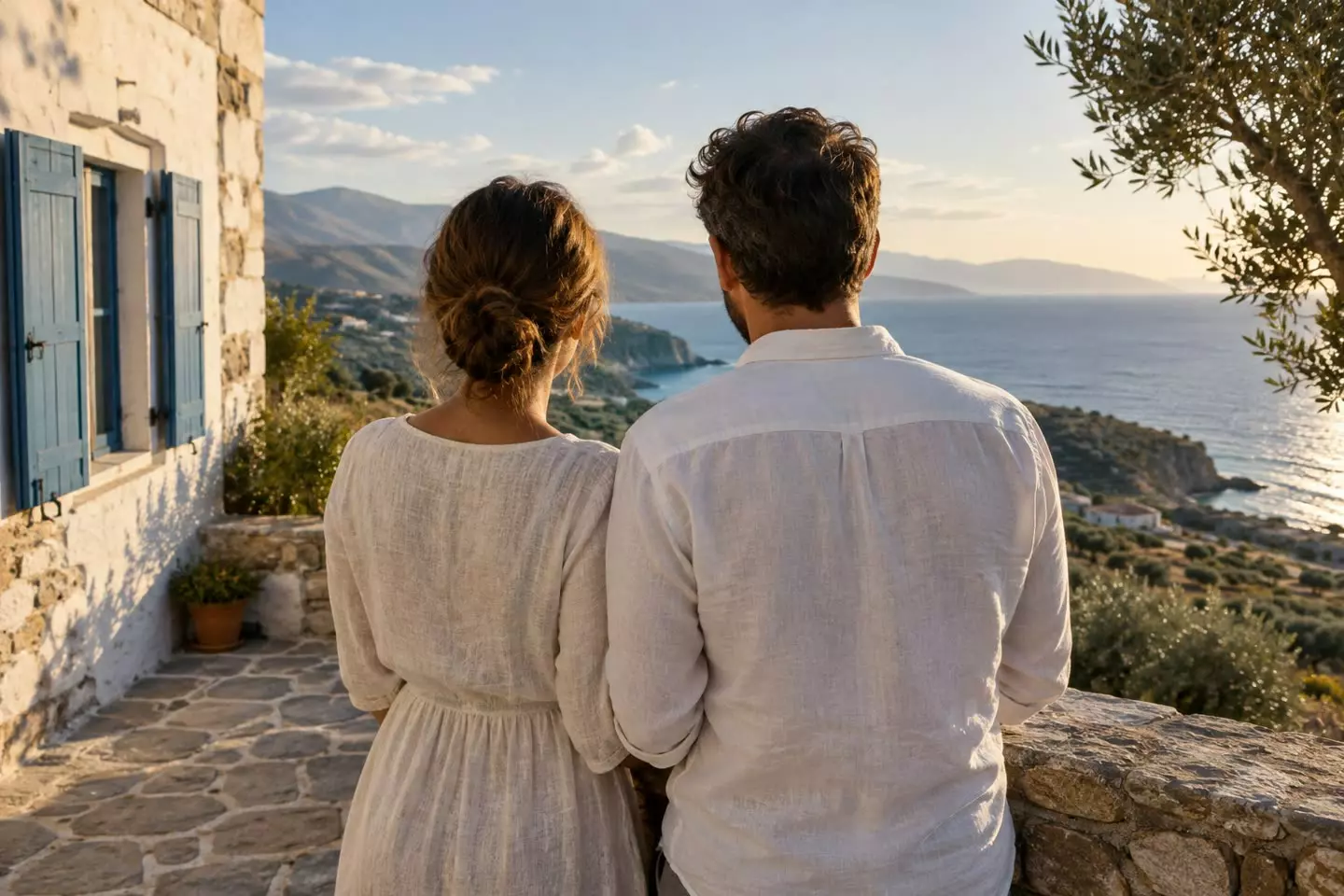 A couple seen from behind looking out to sea from the stone terrace of a whitewashed house in Crete, Greece, in early October (illustration)