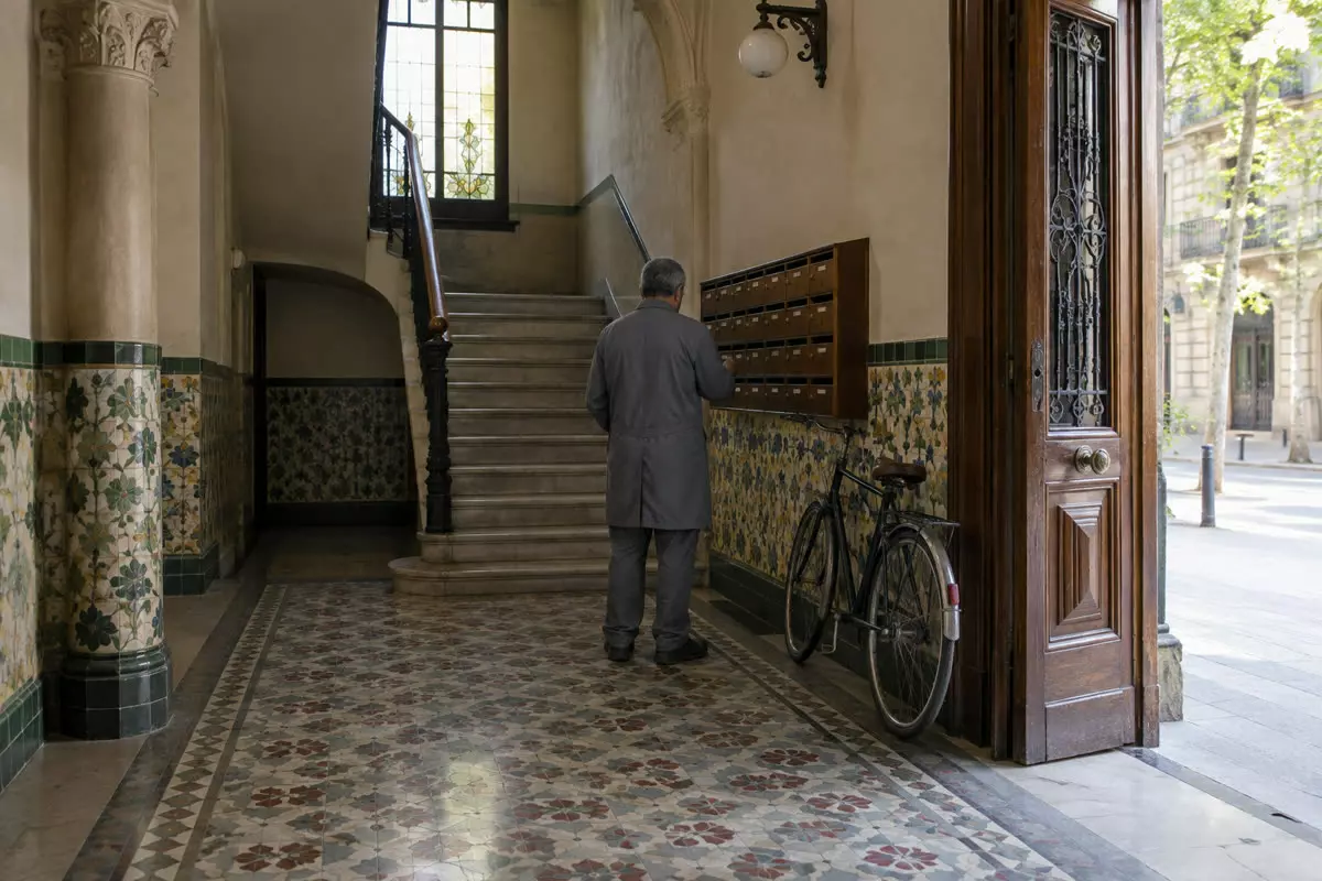 A caretaker seen from behind in the tiled entrance hall of an older apartment block in Barcelona, Spain, in early autumn (illustration)